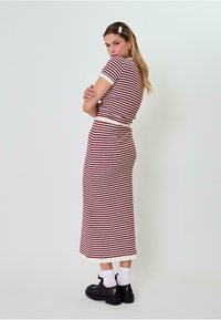 Prugasta pletena haljina s bijelim i burgundskim horizontalnim linijama, kratkim rukavima, prilagođenim gornjim dijelom i lepršavom suknjom. Nosena s crnim cipelama i bijelim čarapama.