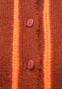 Pruuni kootud kardigan kahe pruuni nupu ja vertikaalsete neoonoranžide triipudega. Tekstuuriga kangas klassikalise nööpidega disainiga.