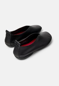 Ballerine nere in pelle con punta arrotondata, design minimalista e interno rosso. Presentano un piccolo occhiello sul tallone per facilitarne l'indossamento.
