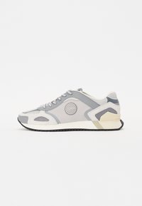 Scarpa sportiva grigia realizzata in materiale mesh e sintetico, con punta rotonda, lacci sulla parte anteriore, dettaglio del logo sul lato e suola in gomma a contrasto.