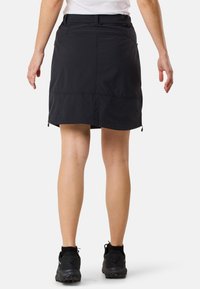 Zwarte rok met een gestructureerde afwerking, met een gestroomlijnde vorm, een verstelbare tailleband en discrete zijritsen. Draagt met zwarte sneakers.