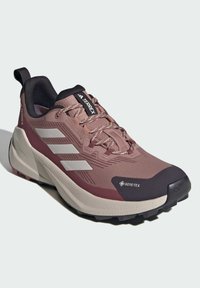 Scarpa da trail GORE-TEX in rosa polveroso e grigio. Presenta tre strisce bianche, tomaia testurizzata, suola ammortizzata e suola esterna nera con trazione robusta.