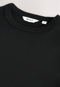 Čierne rebrované tričko s okrúhlym výstrihom vyrobené z mäkkej látky. Má hladkú textúru a etiketu s nápisom "NEXT" blízko krku.