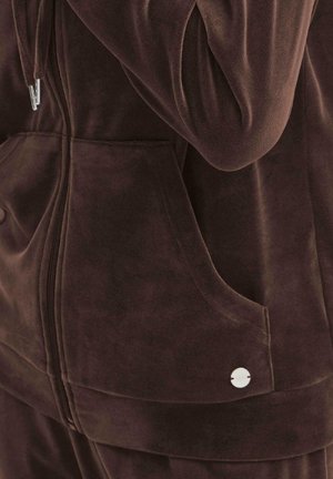 Brown velour zip-up jacket with front pockets, subtle sheen, and metal accent button near the pocket. Soft, textured fabric.
