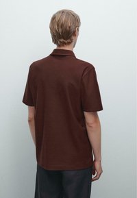 Brun polo tröja med klassisk krage, korta ärmar och avslappnad passform. Tyget ser slätt ut med minimal textur och detaljer.