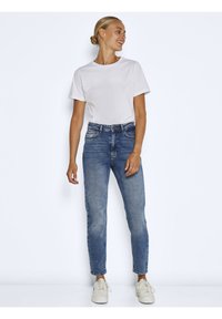 Weißes Rundhals-T-Shirt kombiniert mit jeansblauen, mittel-hohen Jeans. Die Jeans haben eine gerade Passform und einen leichten Used-Look. Helle Sneakers runden den Look ab.