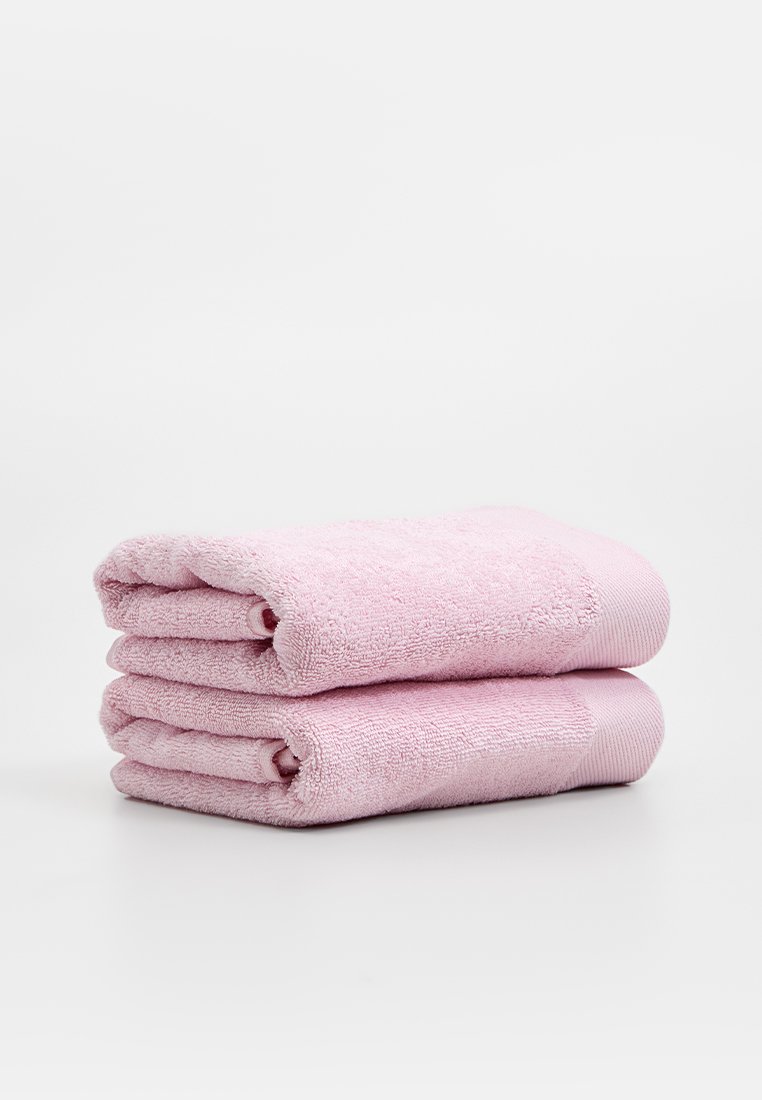 Deux serviettes de bain empilées en rose clair, fabriquées en éponge douce avec une texture moelleuse et un détail côtelé sur les bords.