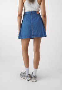 Jeanskjol med en utfläxad form, medellång fåll och en brun läderlapp på midjan, i kombination med grå sportskor.