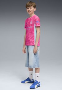 Rosa och ljusblå kortärmad t-shirt med ett texturerat mönster, tillsammans med ljusa jeansshorts och blå sneakers.