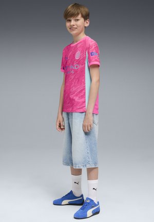 Rosa und hellblaue Kurzarm-Jersey mit strukturiertem Muster, kombiniert mit hellen Denim-Shorts und blauen Turnschuhen.