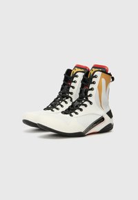 Stivali da boxe alti bianchi e neri con pannelli in rete, dettagli dorati, suola nera piatta e lacci neri. Presenta il marchio sul lato.