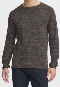 Strickpullover mit langen Ärmeln in dunkelblau und braunem Melangemuster, ausgestattet mit einem gerippten Ausschnitt und Ärmeln, und einem kleinen braunen Lederschild am Saum.