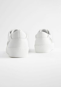 Sneakers bianchi con tomaia in pelle liscia, suola in gomma spessa e dettagli di cucitura semplici. La parte posteriore presenta un tacco arrotondato e un design minimale.