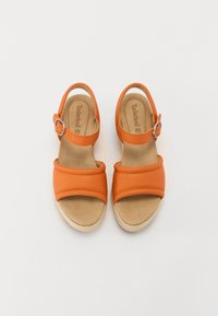 Oransje skinnsandaler med to brede stropper og en ankelstropp med en metallspenne. Myk beige innersåle og teksturert lys såle.