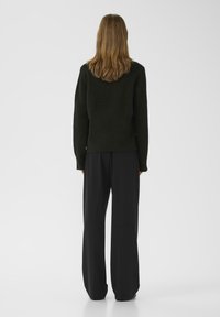 Black long-sleeve sweater made of soft, textured fabric, paired with wide-legged black trousers. The outfit features a relaxed fit and simple design.