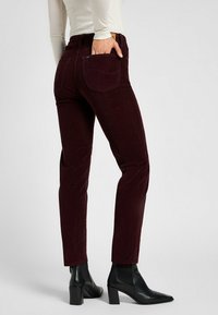 Burgundy corduroy pants with a slim fit, featuring back pockets and a smooth texture, paired with black heeled ankle boots.
