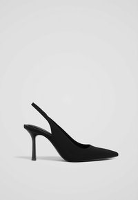 Chaussure à talons hauts noire à bout pointu et bride arrière avec un talon aiguille fin sur un fond gris clair uni.