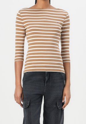 Top de manga larga con rayas marrones y blancas, con escote bote, hecho de tela suave. Combinado con pantalones cargo negros con bolsillos laterales.