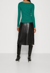 Haut vert à manches longues côtelé associé à une jupe en cuir noire mi-longue et des bottes noires à talons montantes jusqu'au genou. Texture lisse et coupe ajustée.