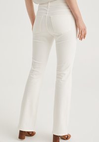 White flared jeans made of denim, featuring a high waist, two back pockets, and a smooth texture, paired with brown heeled sandals.
