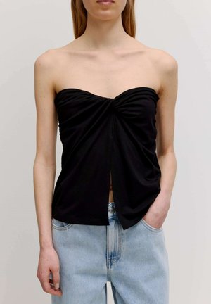 Schwarzes trägerloses Top mit Raffung in der Mitte und einem geschlitzten Saum. Kombiniert mit hellblauen Jeans, die einen lässigen Schnitt zeigen.