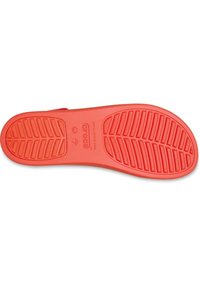 De rode rubberen zool van een Crocs-sandaal heeft een gestructureerd loopvlakpatroon voor grip, met een reliëflogo en maatdetails nabij het hielgedeelte.