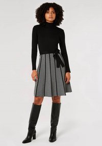 Haut à col roulé noir à côtes associé à une jupe à motifs chevron noir et blanc de longueur genou. Bottes en cuir noir montant jusqu'aux genoux.