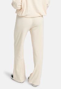 Crèmekleurige geribde flare pants met een zachte textuur en een relaxte pasvorm, gecombineerd met zwarte sneakers. Duidelijk zichtbare naden langs de zijkanten.