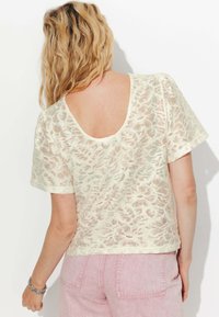 Haut en dentelle blanche à manches courtes et dos plongeant. Présente un motif floral et une coupe décontractée. Associé à un pantalon rose clair.