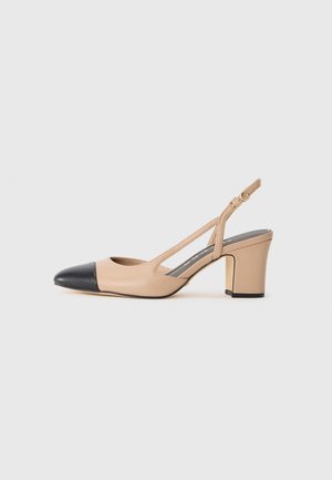 Scarpa slingback beige con punta nera, tacco a blocco e cinturino con fibbia dorata su uno sfondo bianco semplice.