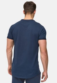 Navyblaues T-Shirt mit kurzen Ärmeln, abgerundetem Saum, Rundhalsausschnitt und einfachen Nähdetails. Hergestellt aus einem glatten, leichten Baumwollmaterial.