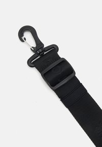 Zwarte nylon band met een plastic gesp en een metalen haak. Platte textuur, ontworpen voor een veilige bevestiging. Bevat merknaam op de band.