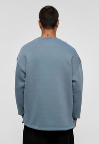 Blauwe sweatshirt met een ontspannen pasvorm, geribde halslijn en manchetten, gemaakt van zachte, textuurrijke stof. De onderkant is iets langer aan de achterkant.