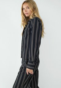 Schwarz-weiße gestreifte Hemdbluse mit Kragen, Brusttasche und langen Ärmeln, kombiniert mit passenden gestreiften Hosen. Glatte Textur.