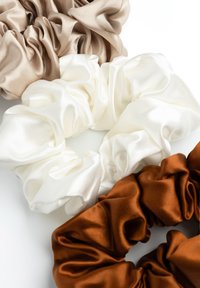 Set van vier zijden scrunchies: lichtbruin, wit en donkerbruin. Gladde textuur, verzameld ontwerp met zachte plooien, in ronde vormen.