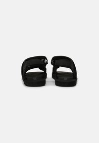 Sandales noires ouvertes à l'arrière avec des straps ajustables, semelles plates et surface texturée. Fabriquées en matériau durable pour le confort et le soutien.