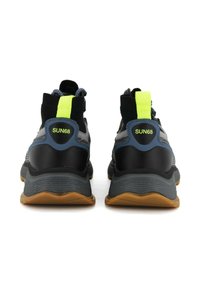 Scarpe sportive nere e grigie con suola in gomma, parte superiore in mesh e dettagli in neon giallo. Presentano il logo del marchio sul tallone e un collare imbottito.