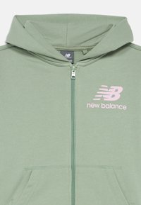 Sweatshirt de capuz verde claro, feito de tecido suave, com um bolso à frente, capuz e um logo rosa "New Balance" no lado esquerdo do peito.