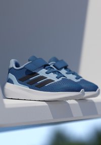 Sinised spordijalatsid võrgukangast, kummist tallaga ja rihmaga. Neil on mustad triibud ja tekstuuriga pind haarduvuse tagamiseks.