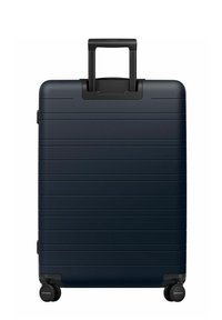 Valise rigide bleu marine avec des rainures horizontales, poignée télescopique et quatre roues noires. Texture lisse, forme rectangulaire, design minimaliste.