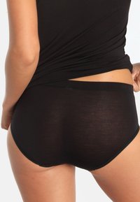 Schwarze Baumwollunterwäsche mit glatter Textur und tief sitzendem Design. Verfügt über einen elastischen Bund und saubere Kanten. Rückansicht gezeigt.