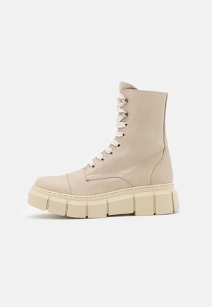 Bottes de combat en cuir beige avec une tige haute, un bout rond, des lacets crème et une semelle beige épaisse et nervurée. Texture lisse avec des accents minimalistes.