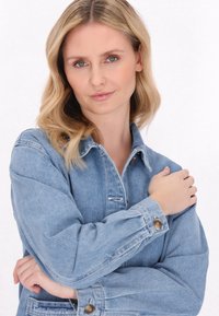 Vaaleansininen denimi takki, jossa on napitettava etuosa, pitkät hihat napilla varustettuina ja rento istuvuus. Sileä pinta.