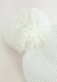 Weißer gestrickter Beanie mit einem großen weißen Pompon oben, ausgestattet mit einem strukturierten Muster und weichem Garnmaterial.