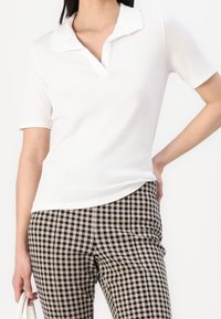 Bílá polokošile s límečkem, vyrobená z lehké tkaniny. Spárována s černobílými kostkovanými kalhotami se slim fit střihem.