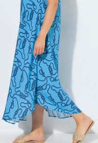 Ljusblå maxiklänning med ett marinblått repmönster, med en flödande design och genomskinlig fåll. Bärs med beiga slip-in-sandaler prydda med detaljer.