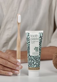 Bamboe tandenborstel met witte haren naast een tube tandpasta met een teal- en zwart patroon, gemerkt "tandpasta" met "kokosnoot en zink."