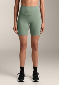 Vysoké zelené cyklistické šortky vyrobené z elastického materiálu, s hladkou textúrou a čistým dizajnom bez viditeľných vzorov.