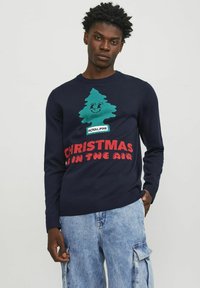 Der marineblaue Pullover zeigt ein grünes lächelndes Baum-Graphic mit dem Label "ROYAL PINE" und dem Text "CHRISTMAS IN THE AIR" in Rot. Hergestellt aus gestricktem Stoff.