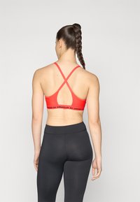 Röd sport-bh med korskonstruktion bak, prydd med ett brett svart band med texten "Under Armour". Matchas med svarta högmidjade leggings.